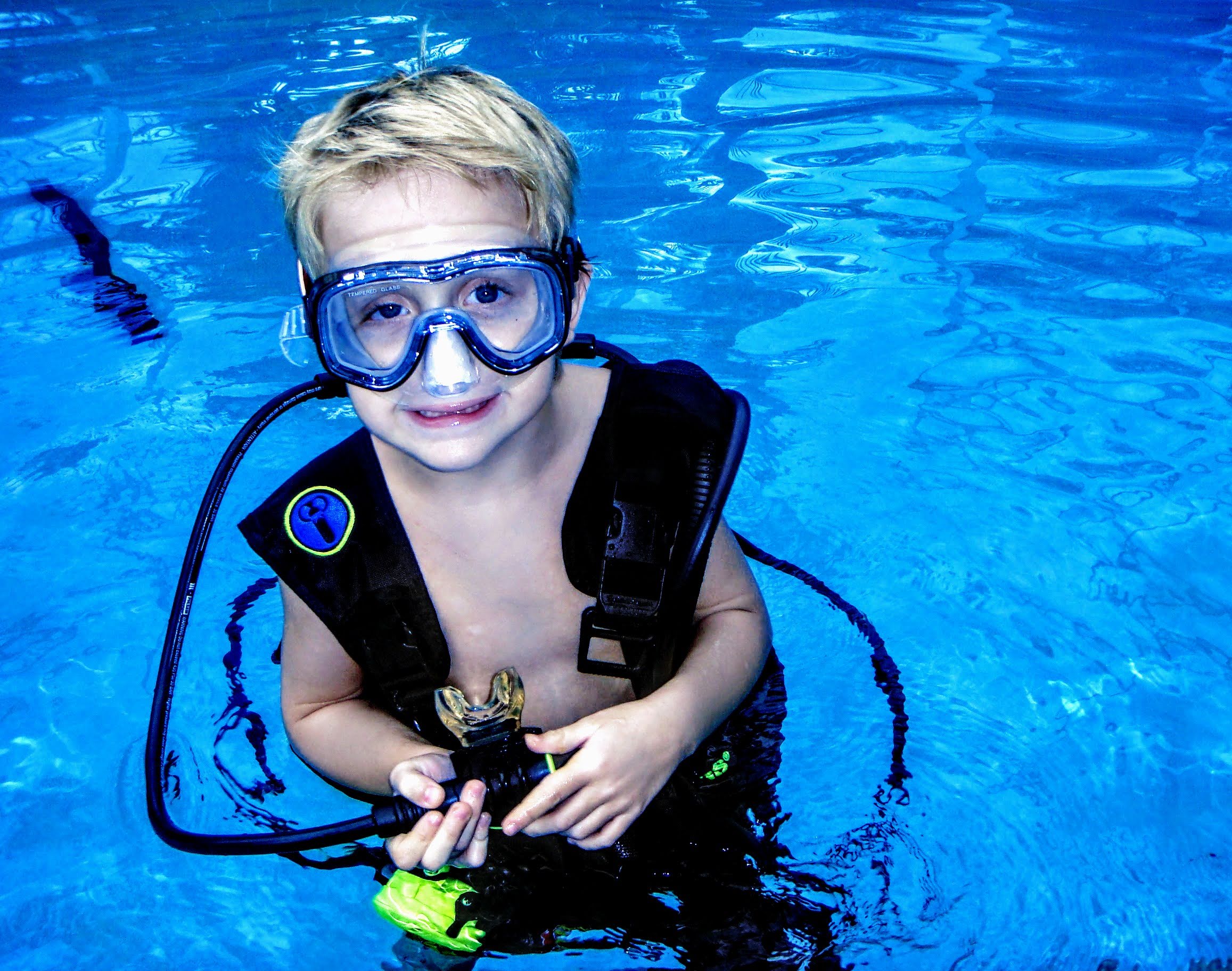 Young diver smiling in clear blue water while wearing a mask and buoyancy vest